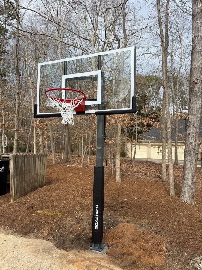Goliath in-ground basketball hoop installed at the edge of a wooded backyard