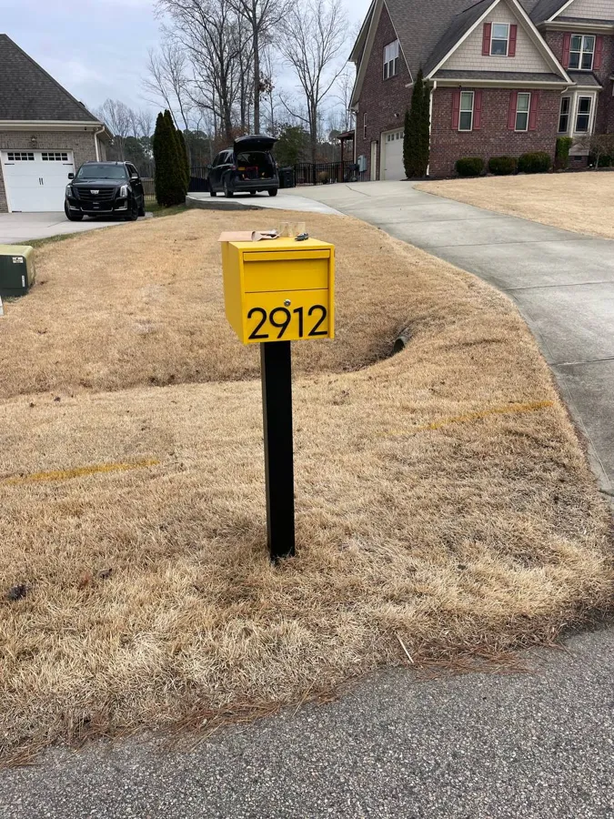 Yellow mailbox with the house number, set on a new black post at the end of a driveway